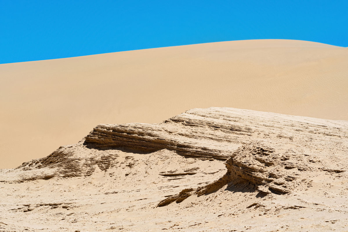 Литифицированные песчаные отложения на фоне песчаной дюны в пустыне