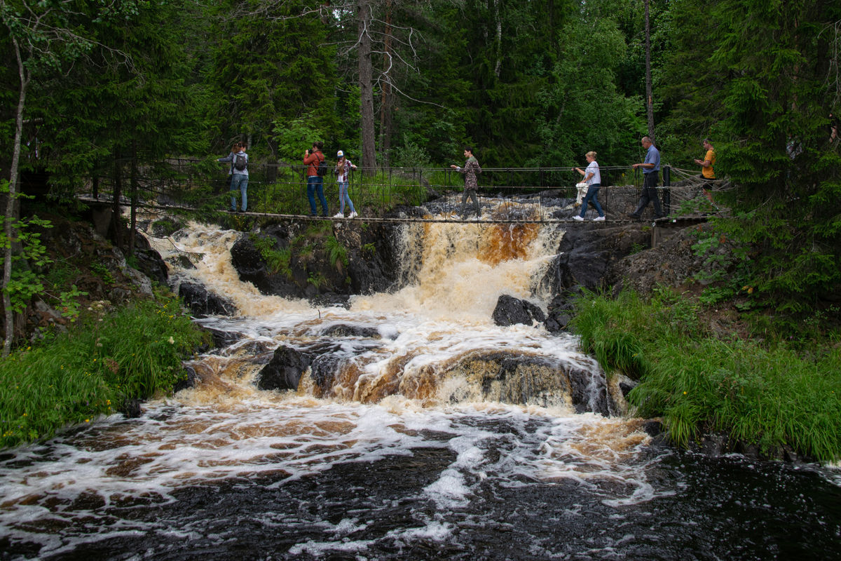 Туристы идут по мосту мимо Рускеальского водопада