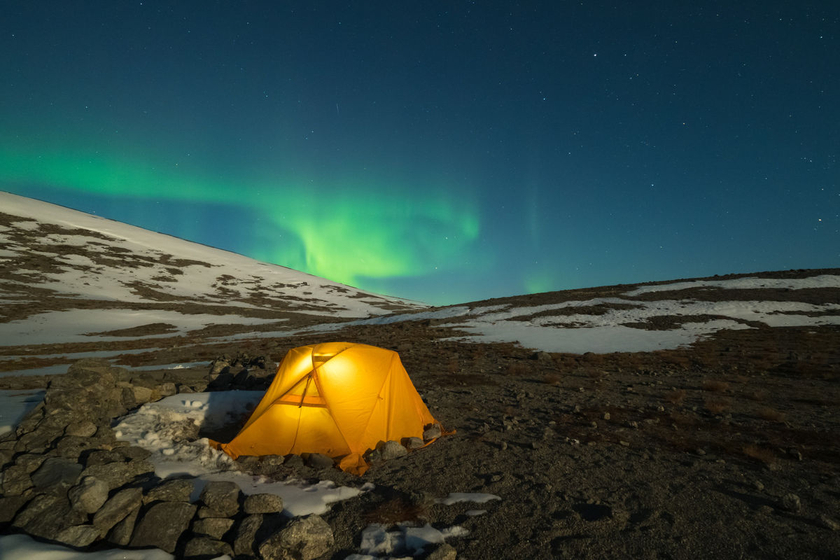 Ночное звездное небо и зеленое северное сияние над светящейся желтой палаткой в Хибинах