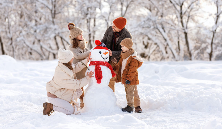 Счастливые дети лепят веселого снеговика вместе с родителями