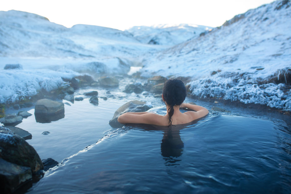 Девушка купается в источнике с видом на заснеженные горы